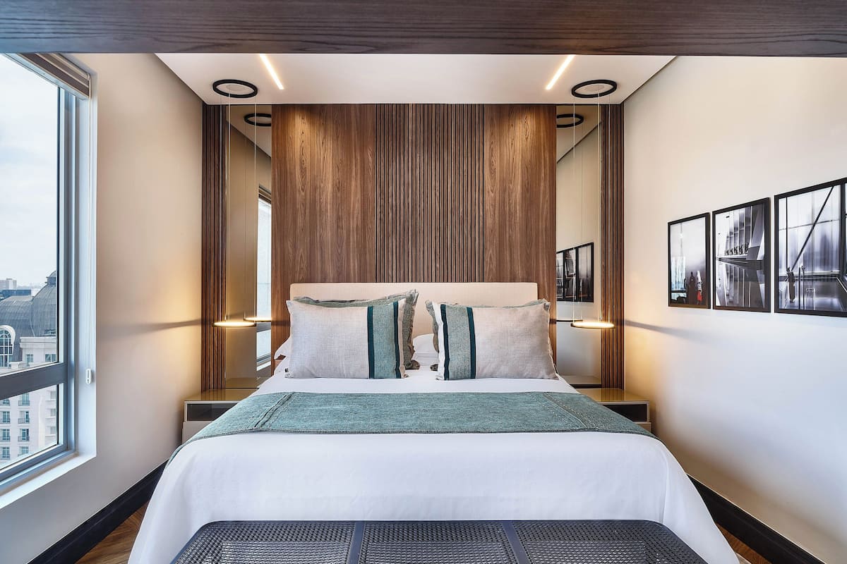 A modern hotel room with a large bed, wooden panel wall, and city views.