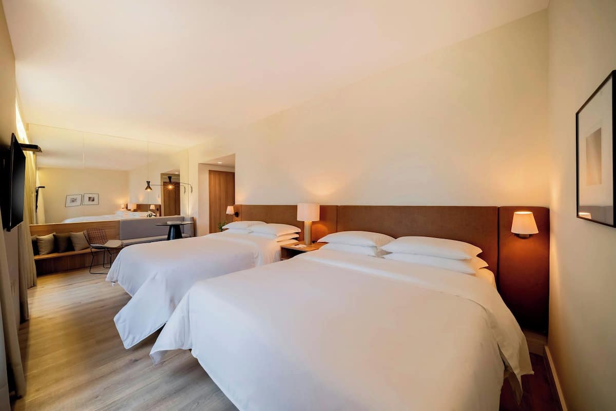 A hotel room with two beds, a desk, and a seating area.