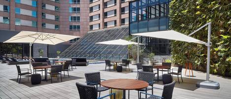 Una terraza en la azotea con mobiliario exterior, piscina y vista a un edificio alto.