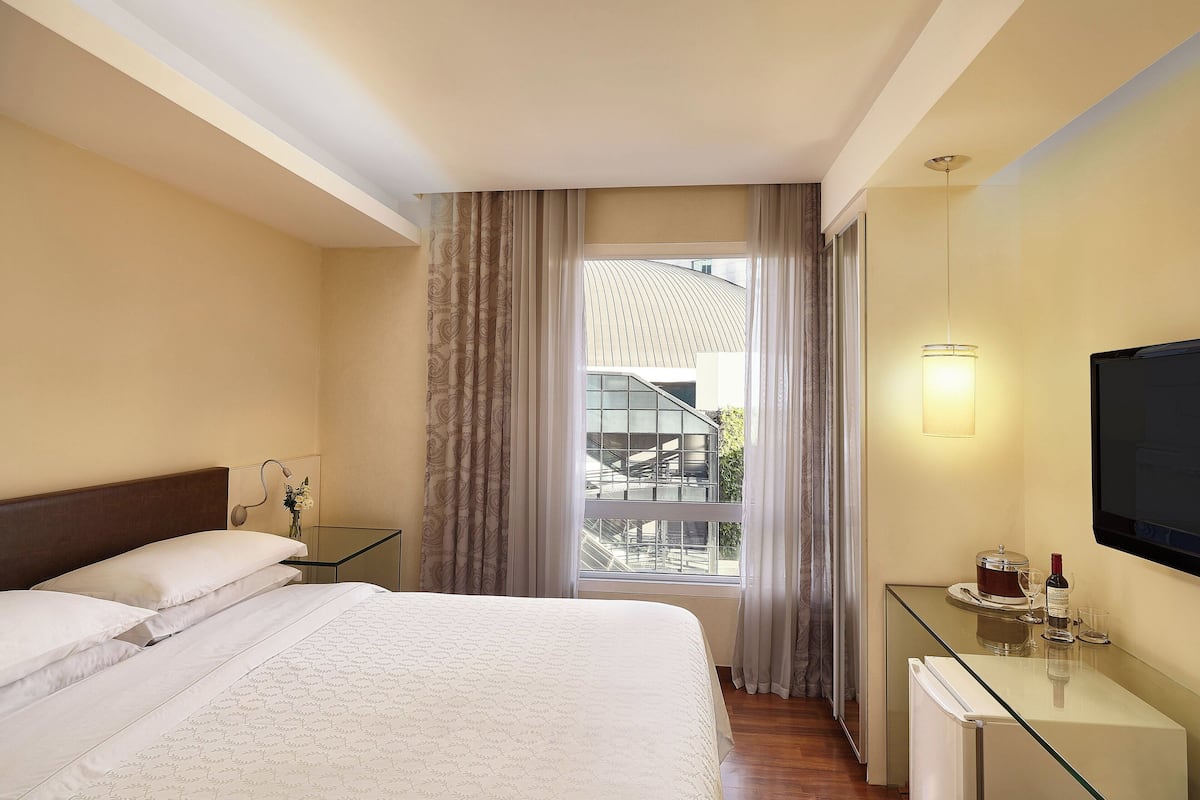 A hotel room with a bed, a glass desk, a television, and a window with curtains.