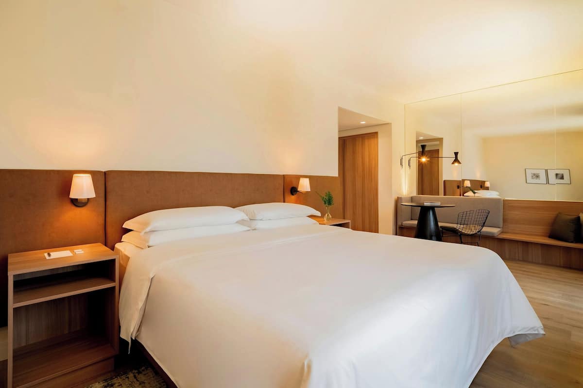 A hotel room with a large bed, bedside tables, a desk, and a mirror.