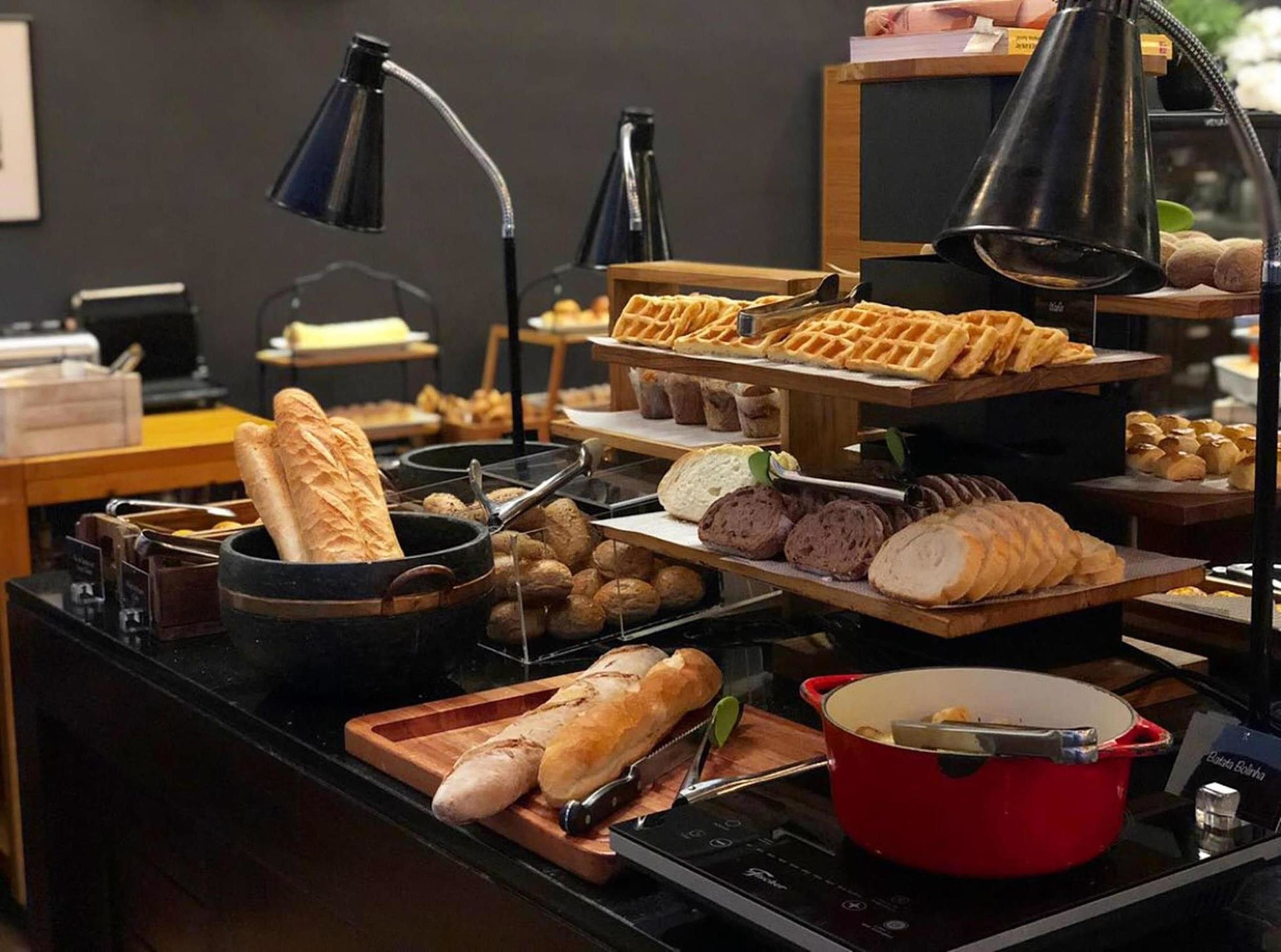 En buffé med olika sorters bröd och bakverk, och en röd kastrull på en avställningsyta.
