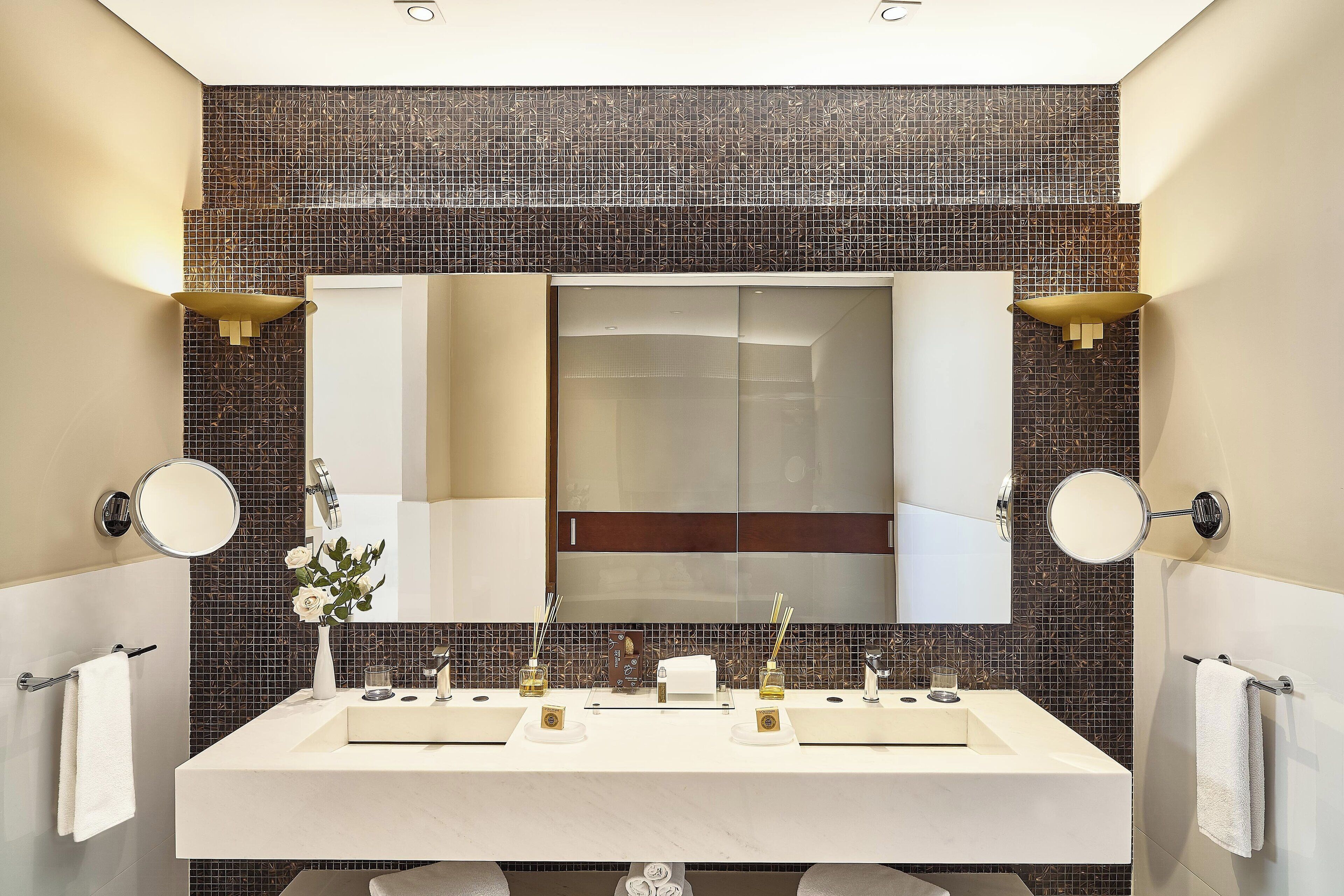 A modern bathroom with a large mirror, two sinks, and a decorative tile backsplash.