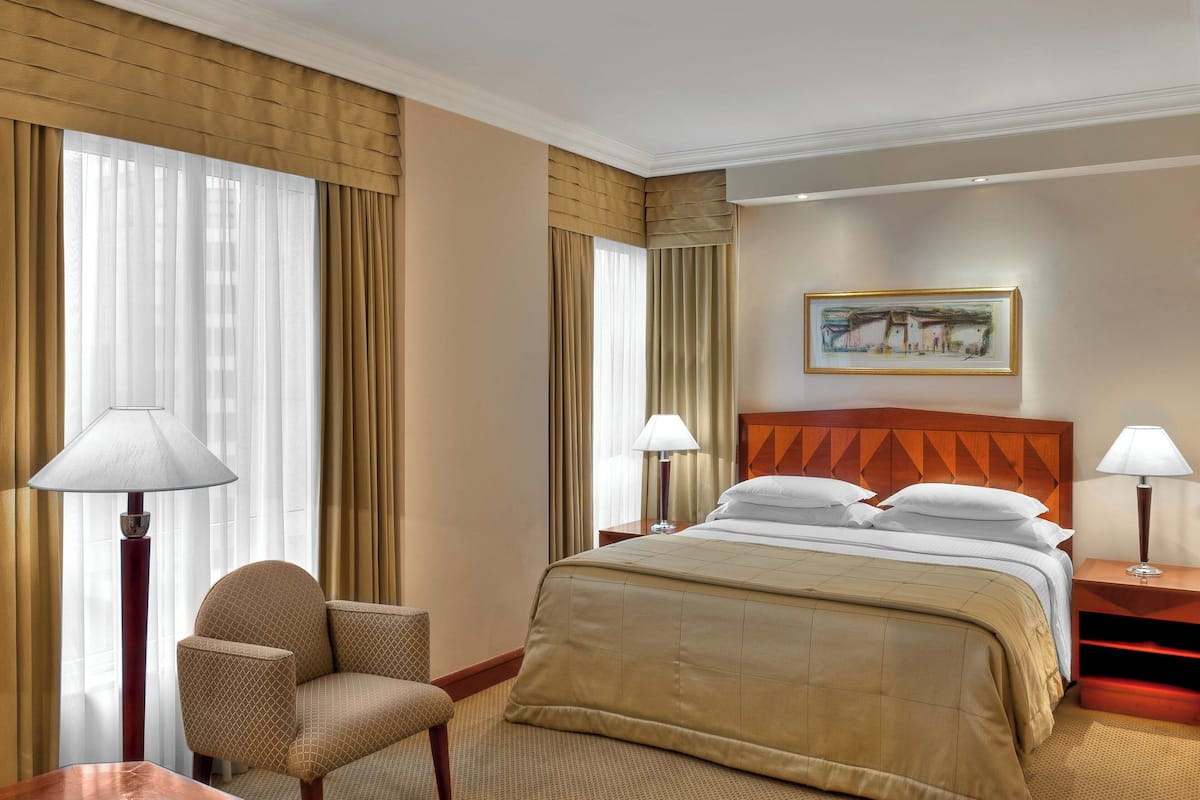 A hotel room with a large bed, two bedside tables with lamps, a chair, and a painting on the wall.