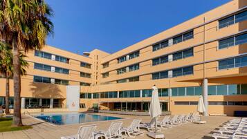 Un hotel con piscina, tumbonas y una palmera.