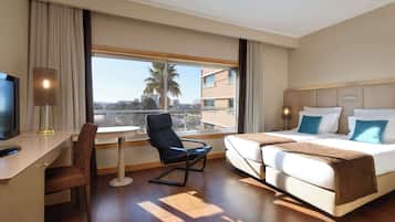Une chambre d’hôtel équipée d’un bureau, de deux lits, d’une chaise et d’une grande fenêtre donnant sur la ville.
