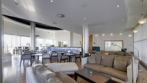 A spacious lounge area with modern furniture, a bar in the background, and large windows offering a city view. - TRYP by Wyndham Porto Expo Hotel (Matosinhos)