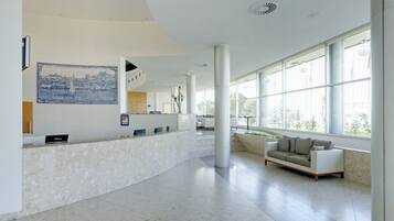 Um hall amplo com balcão de recepção, uma janela grande com vista e um sofá moderno branco.
