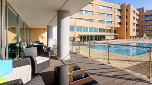 A poolside area with wicker furniture and a view of a hotel building. - TRYP by Wyndham Porto Expo Hotel (Matosinhos)