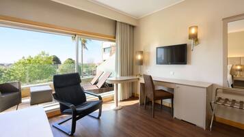 Een hotelkamer met een groot raam, een bureau, een stoel, een televisie en een klein tafeltje.