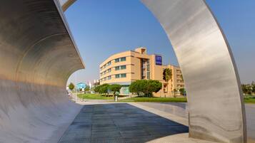 A modern building with a curved metallic structure in the foreground, a sign for TRYP Hotels, and a clear blue sky.