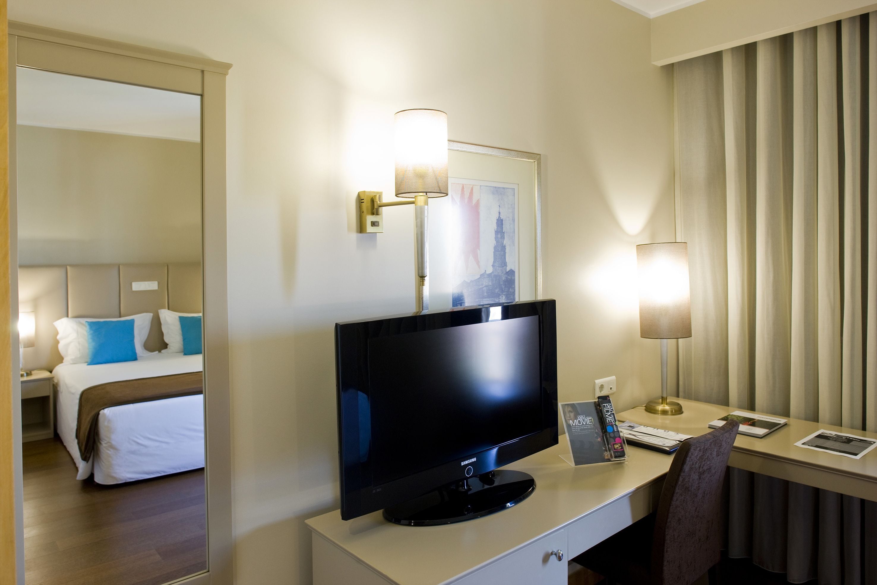 Una habitación de hotel con una cama, un escritorio con una computadora, un televisor y dos lámparas.