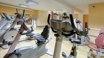 Una palestra con diverse macchine per esercizi, tra cui tapis roulant e cyclette, disposte in file.