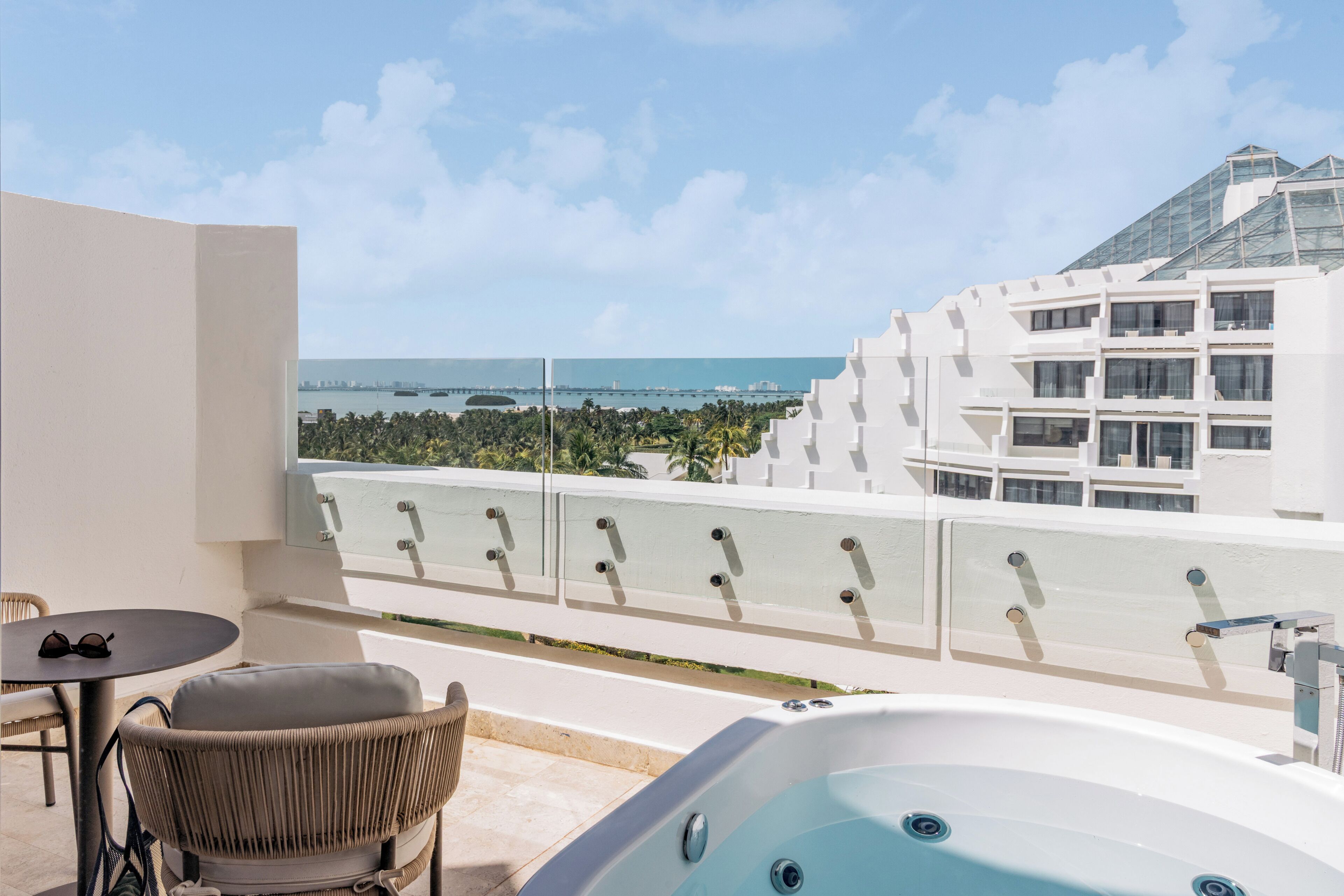 Uma varanda com hidromassagem, cadeira de vime e mesa, com vista para a cidade e o oceano.