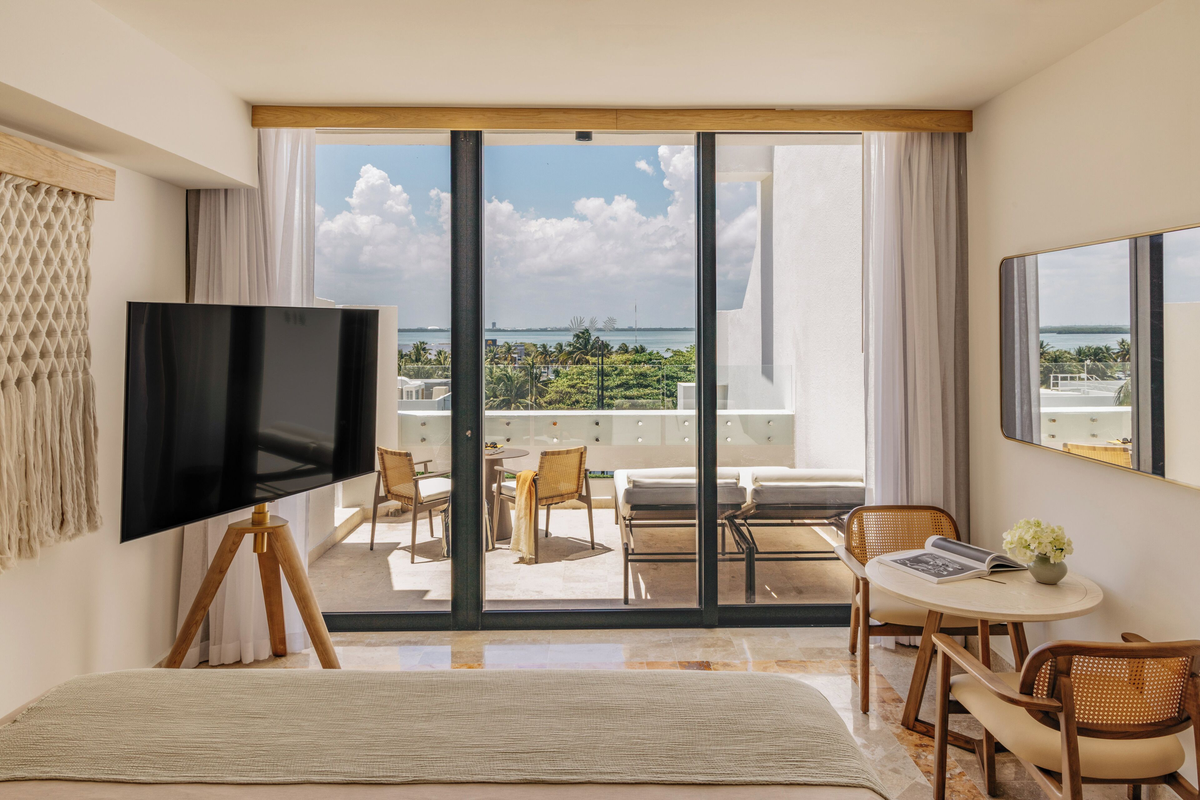 A hotel room with a large TV, a balcony with chairs and a table, and a view of the ocean.