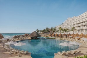 A resort pool with lounge chairs and umbrellas, a thatched hut, and a hotel building with balconies. - Paradisus Cancún – All Inclusive (Cancun)