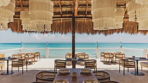 A seaside restaurant with thatched umbrellas, wicker furniture, and a view of the ocean. - Paradisus Cancún – All Inclusive (Cancun)