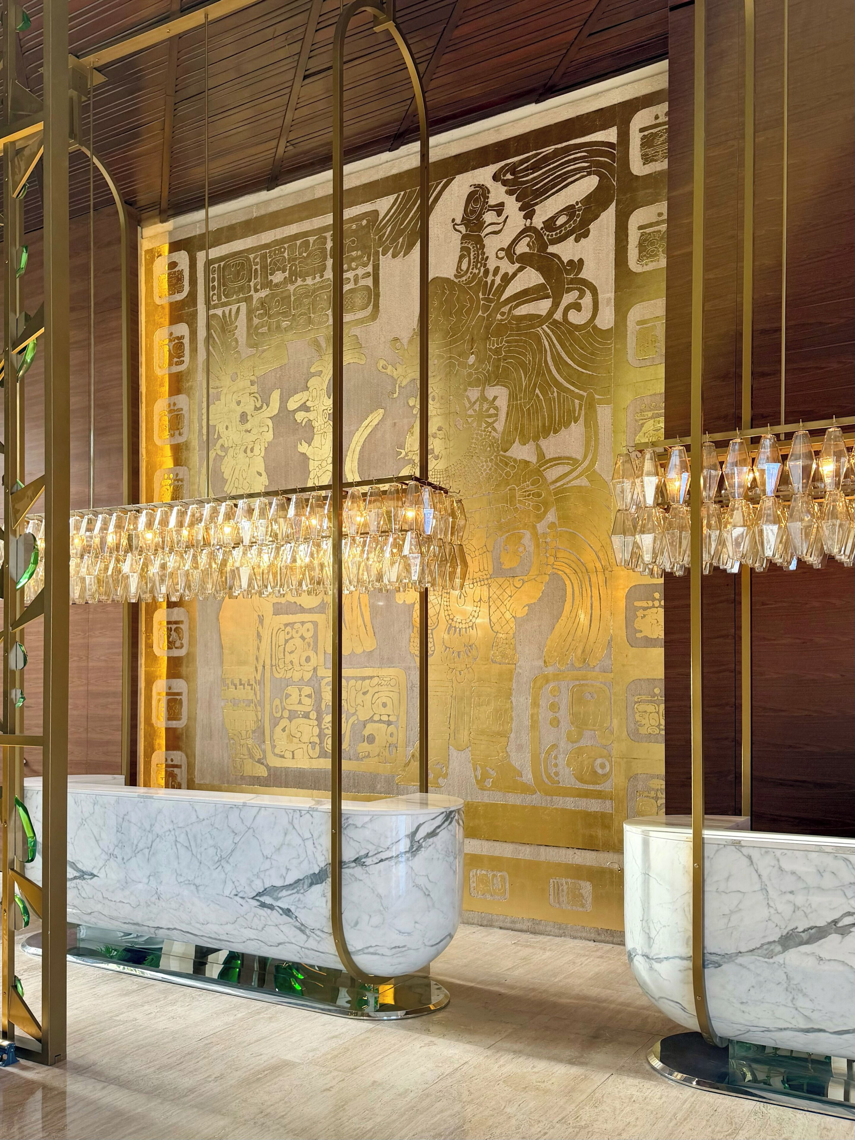 A luxurious bathroom with marble sinks, a decorative wall mural, and a unique chandelier.