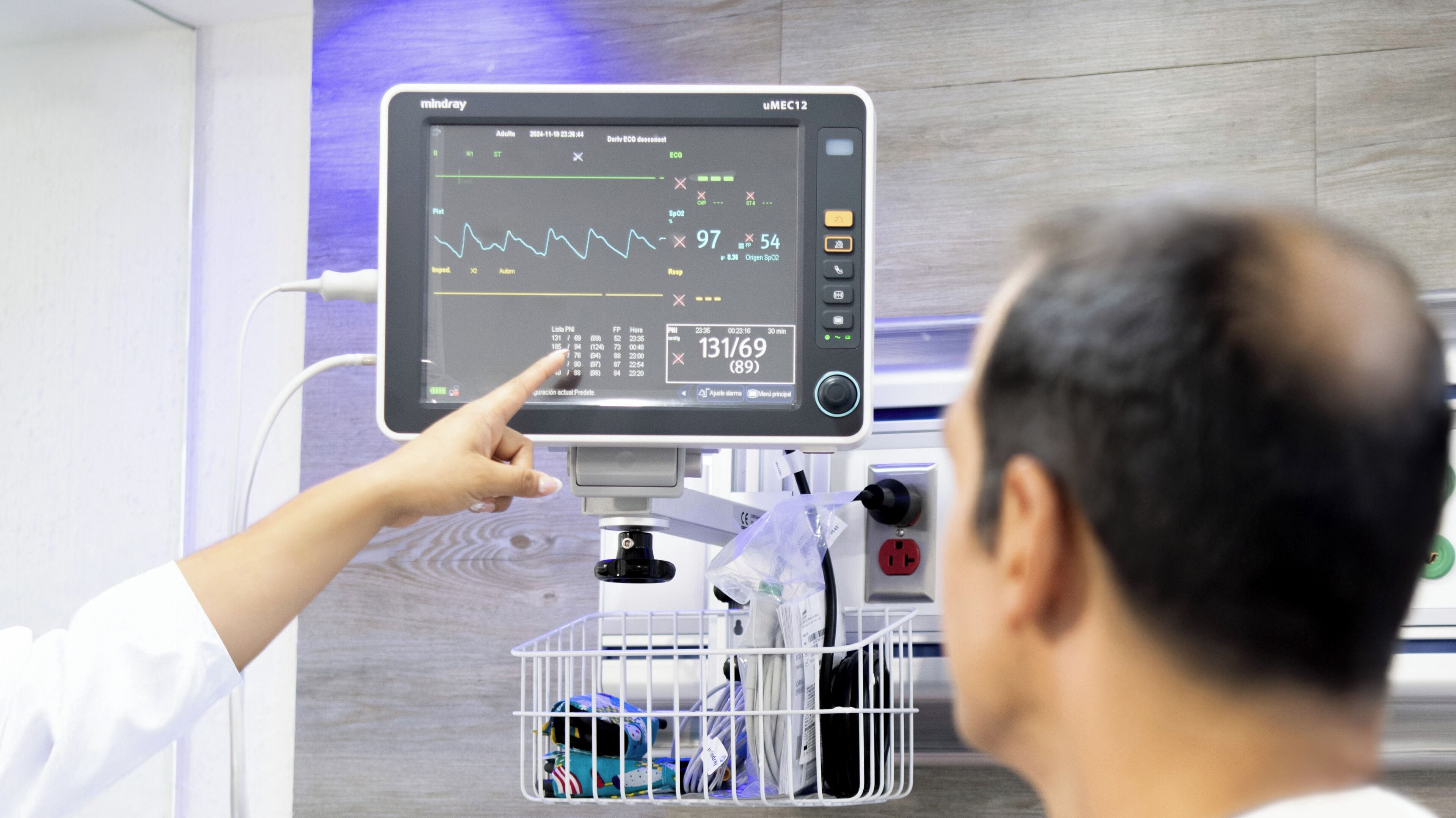 Dispositivo de monitoreo médico mostrando signos vitales y una persona señalando la pantalla.