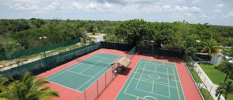 A tennis court with a net, surrounded by a green fence, and palm trees nearby.