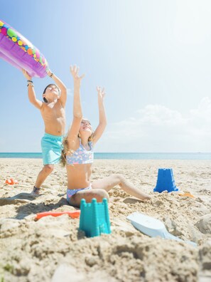 A beach scene with two people playing with a beach ball and sand toys. - Zel Cozumel (Cozumel)