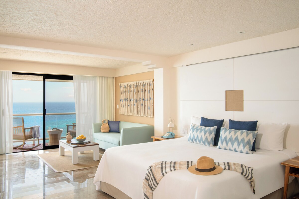 A hotel room with a bed, a seating area with a view, and a large window.