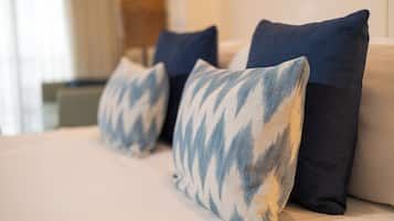 Una cama con tres almohadas, una lámpara y una ventana con cortinas.