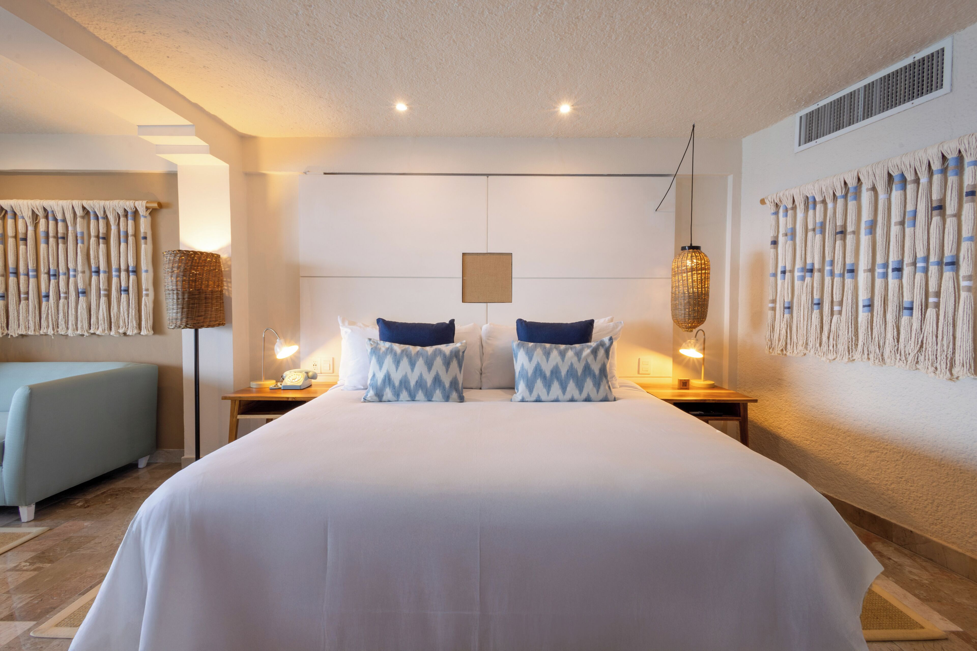 Ein Hotelzimmer mit einem großen Bett, zwei Nachttischen mit Lampen, einem Schminktischchen, einer Couch und einer Wand mit dekorativem Muster.