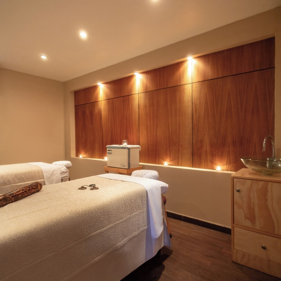 A hotel room with a large bed, bedside tables, a wooden wardrobe, and a small desk with a lamp.