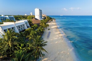 A coastal hotel with a beach view, a pool, and a tall building in the background. - Zel Cozumel (Cozumel)
