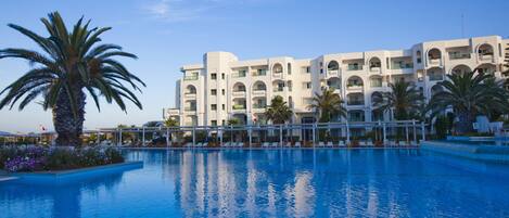 A hotel with a swimming pool, palm trees, and a clear blue sky.
