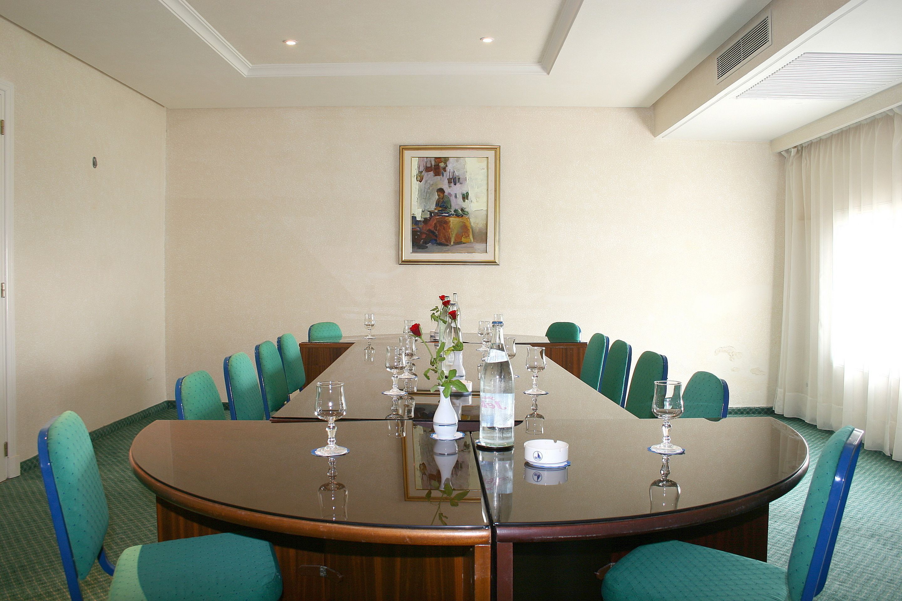 Un salón de conferencias con una gran mesa ovalada, sillas color turquesa y un cuadro en la pared.