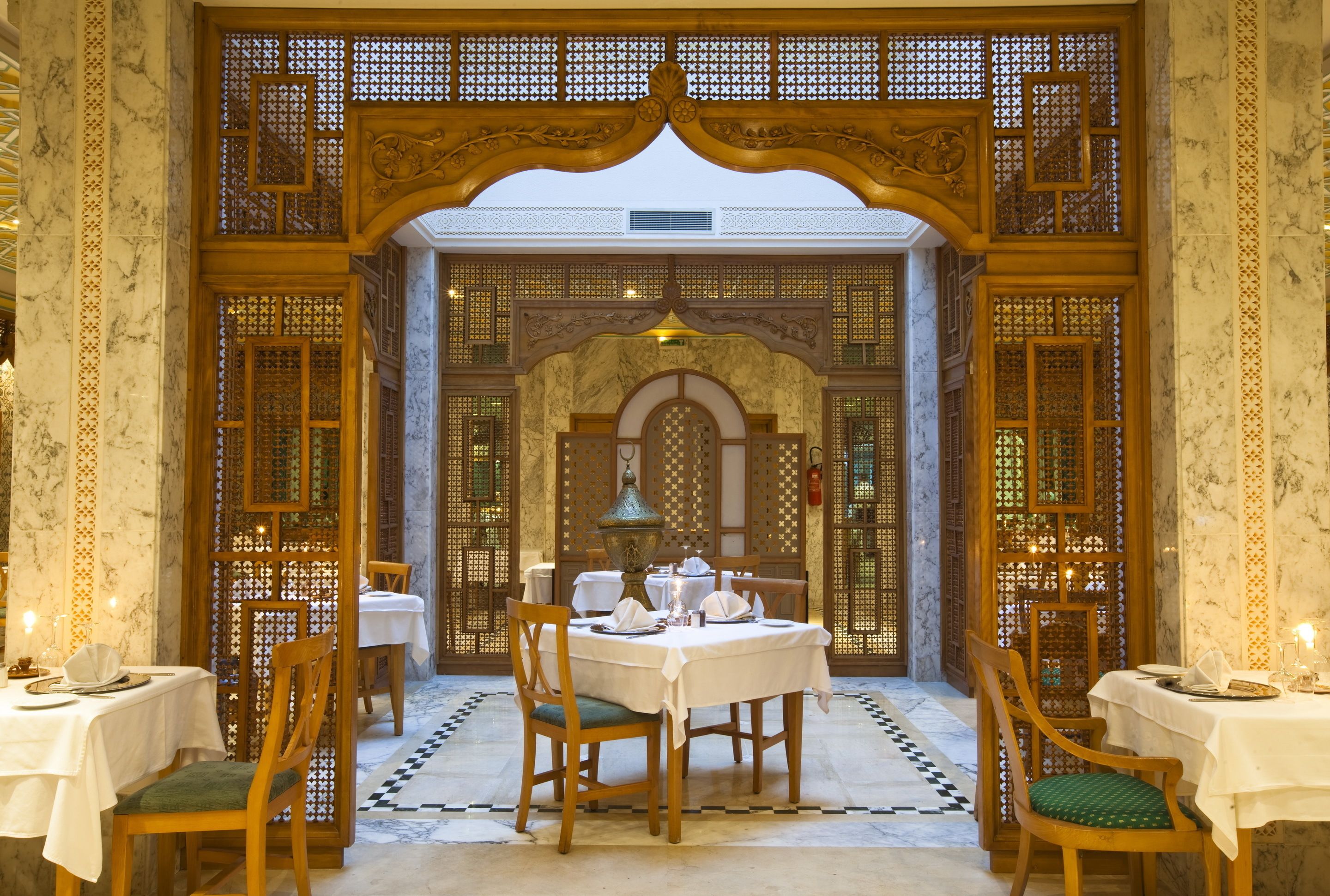 A dining area with tables set for two, wooden chairs, and a decorative archway.