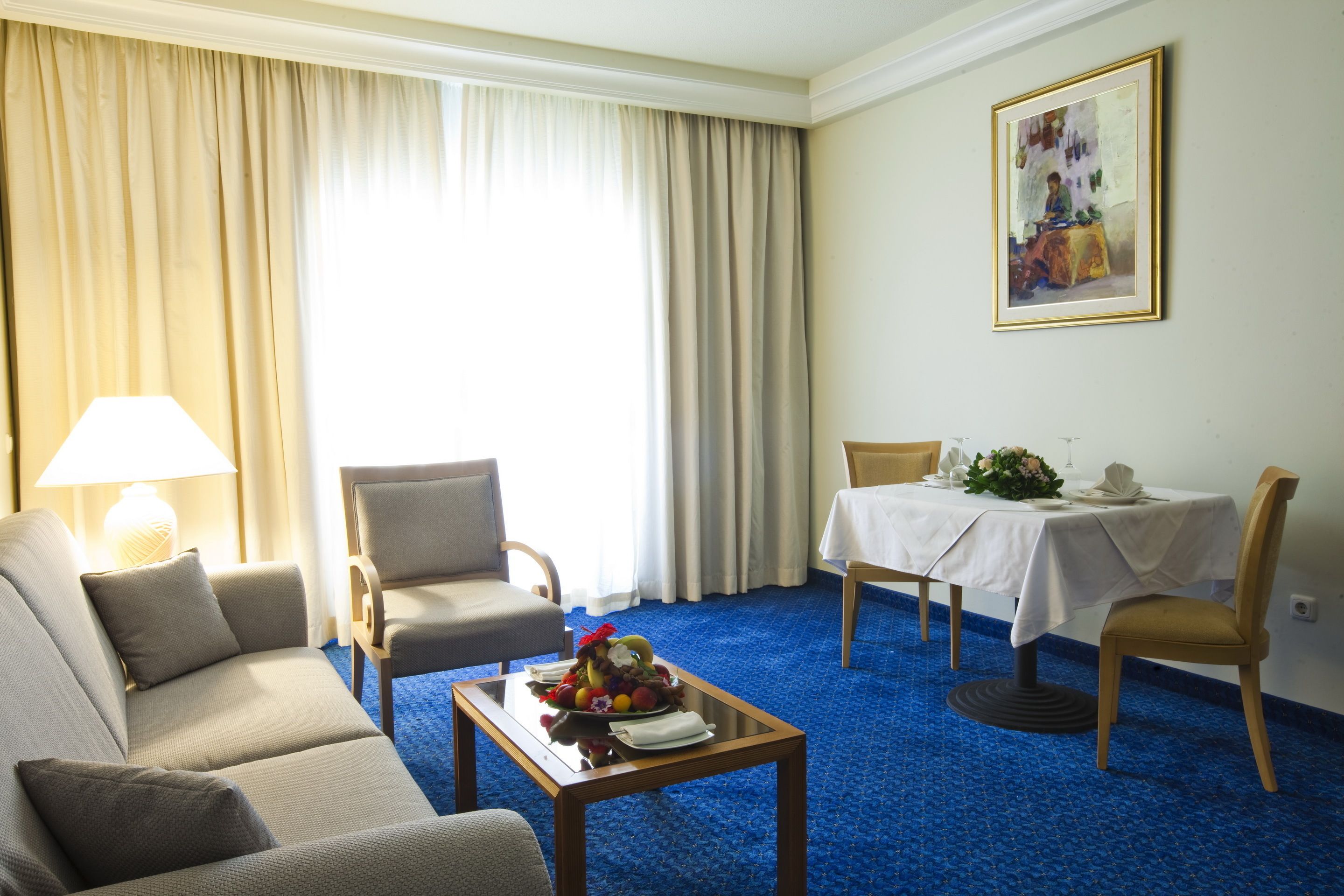 Una habitación de hotel con sofá, sillón, mesa de comedor y un cuadro en la pared.