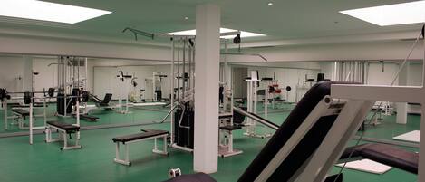 Un gimnasio con diversos equipos de ejercicio, espejos y suelo verde.