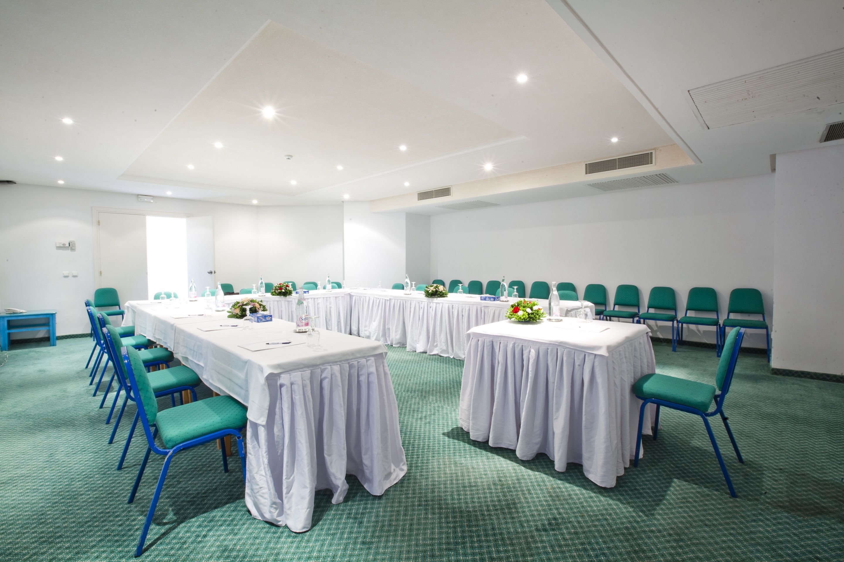 A conference room with long tables, green chairs, and white tablecloths.