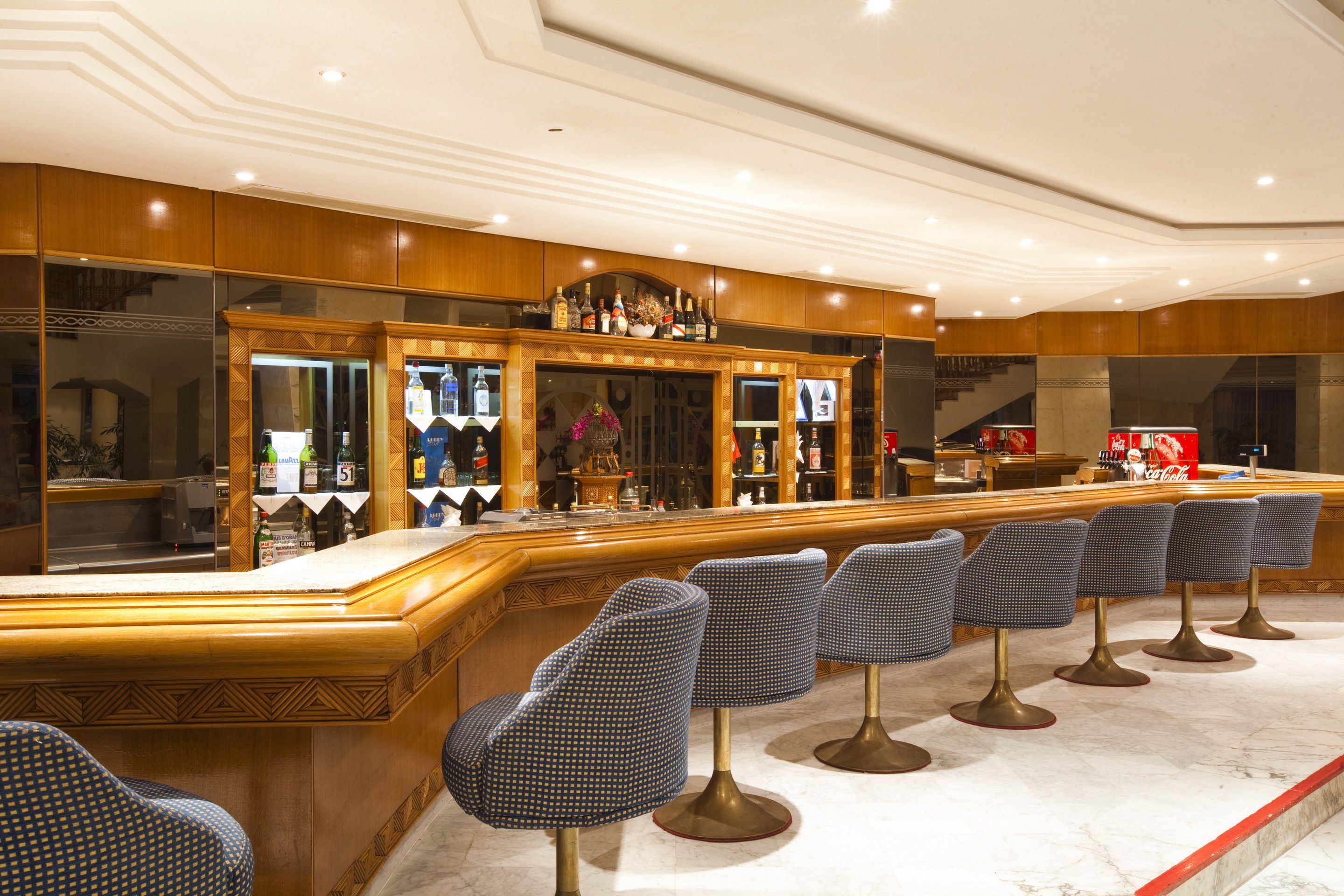 Uma área de bar com bancada de mármore, armários de madeira e banquetas azuis.