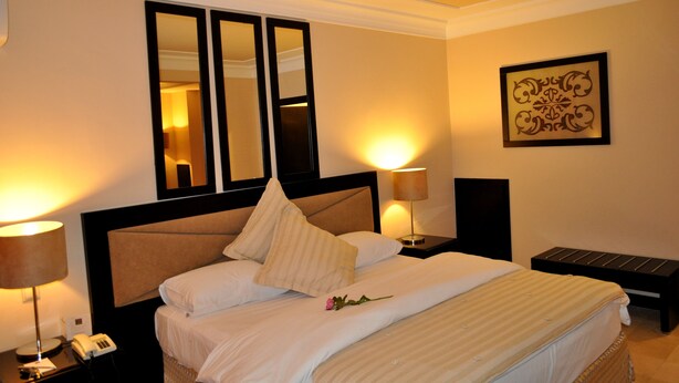 A hotel room with a large bed, two bedside lamps, a bedside phone, a small table, and a decorative wall piece. - Casablanca Le Lido Thalasso & Spa (Casablanca)
