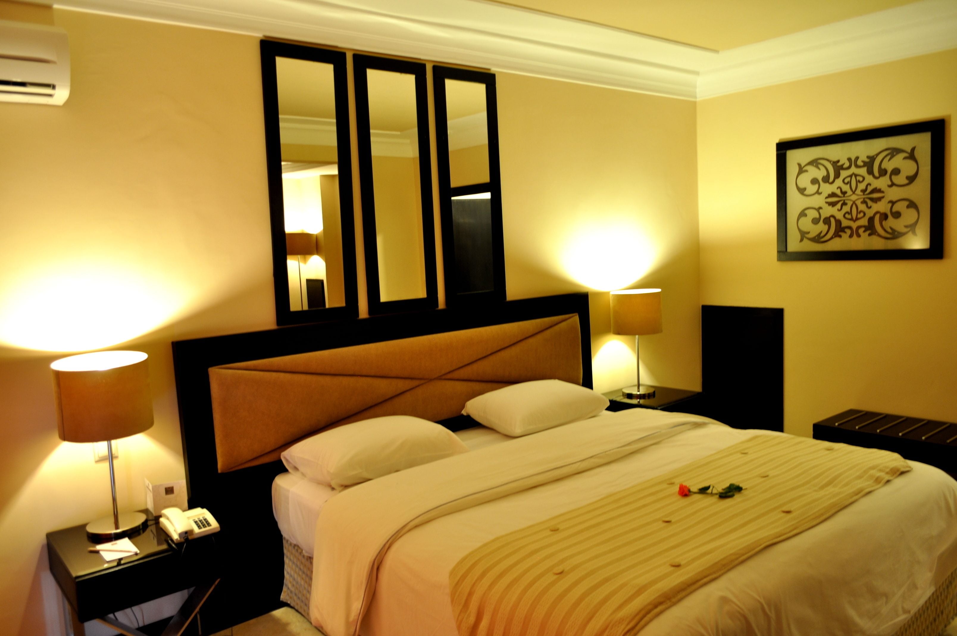 A hotel room with a large bed, two bedside lamps, a mirror, a framed artwork on the wall, and a telephone on the nightstand.