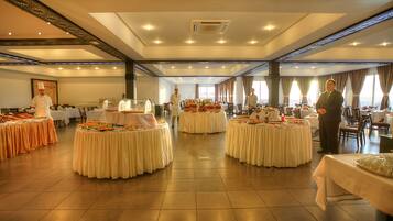 Une vaste salle de banquet dotée de nombreuses tables rondes recouvertes de nappes blanches, disposées selon un agencement symétrique.