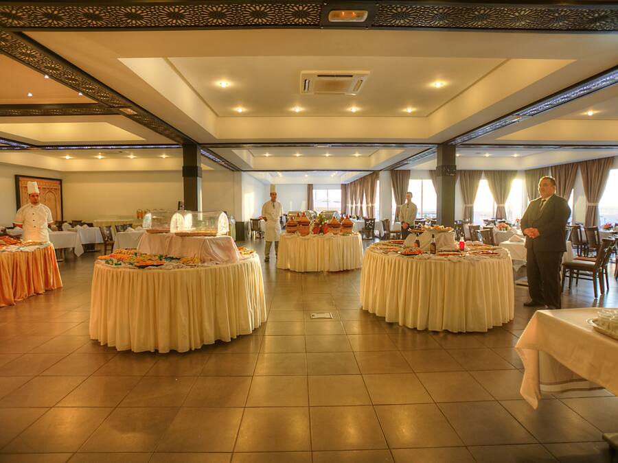Une vaste salle de banquet dotée de nombreuses tables rondes recouvertes de nappes blanches, disposées selon un agencement symétrique.