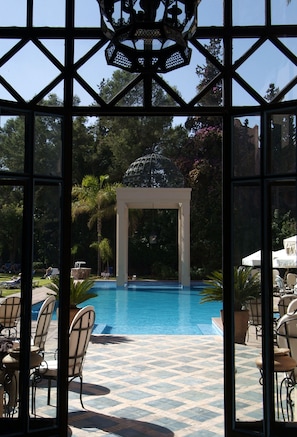 Un área de piscina con una pérgola, sillones de descanso y un patio empedrado.