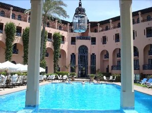 Un espace piscine avec une eau d’un bleu limpide, entouré d’un bâtiment doté d’arcades et de balcons.