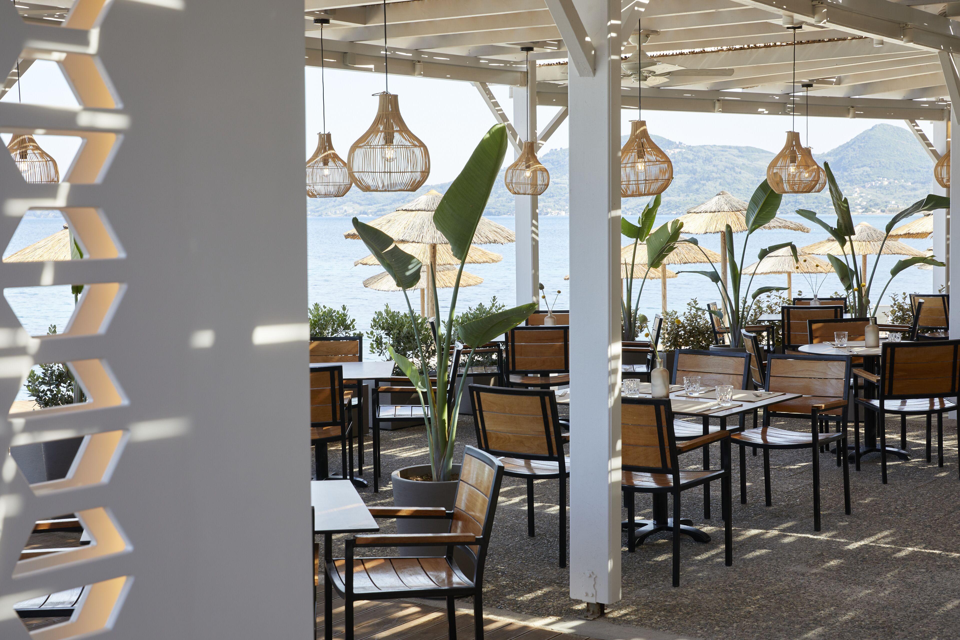 Een terras met tafels en stoelen, grote parasols en hangende lampen.