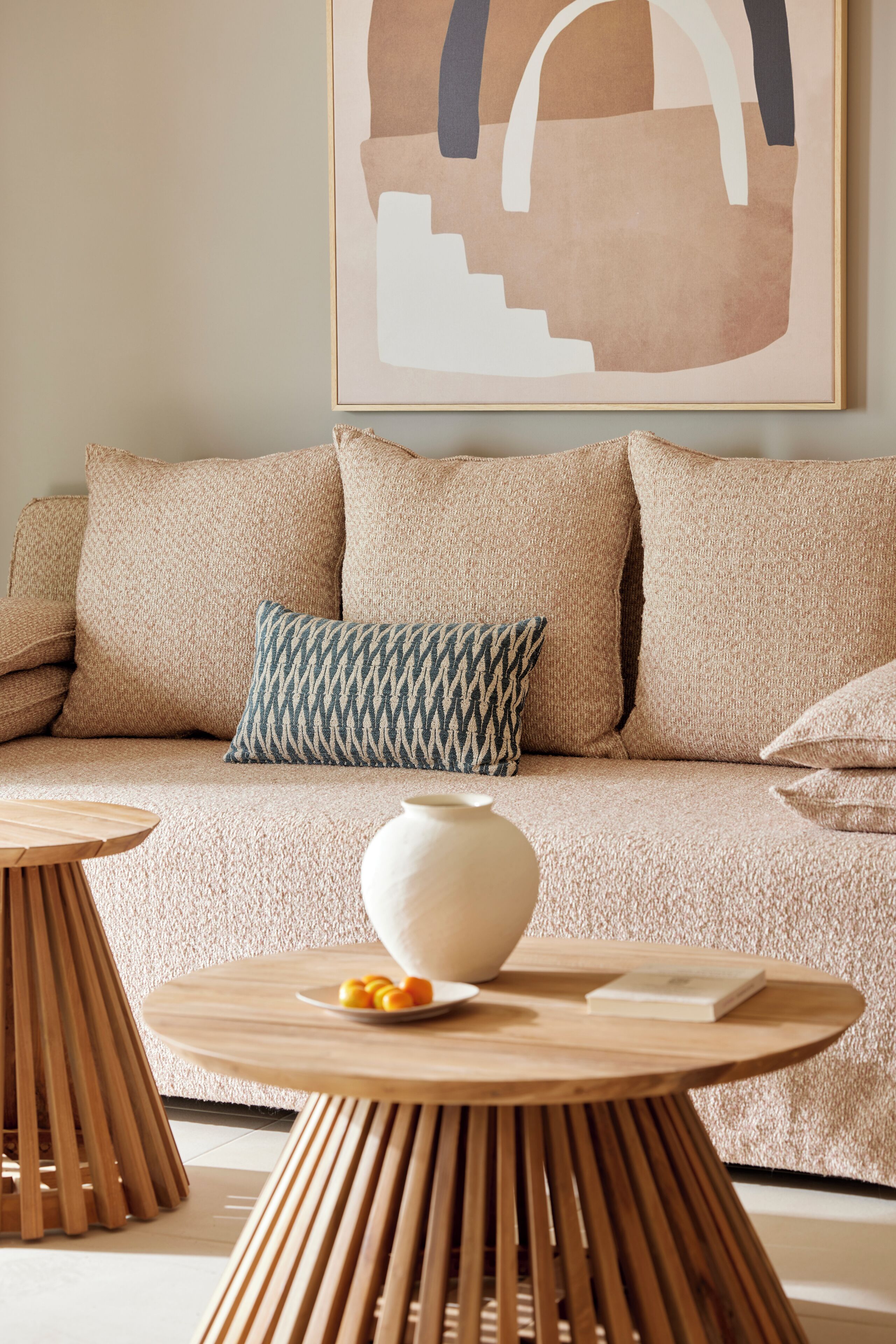 A modern living room with a beige sofa, patterned pillows, a white vase, and wooden side tables.