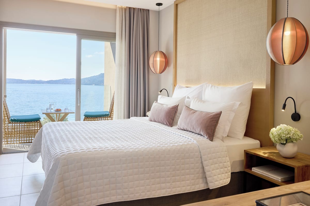 Ein Hotelzimmer mit einem großen Bett, Meerblick und einem Balkon mit Tisch und Stuhl.
