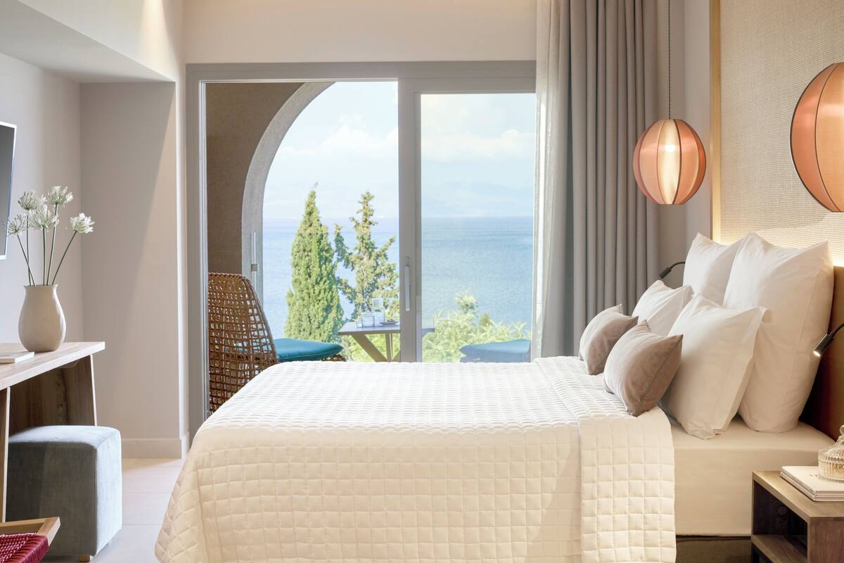 Ein Schlafzimmer mit einem großen Bett, Meerblick und einem Balkon mit Tisch und Stühlen.