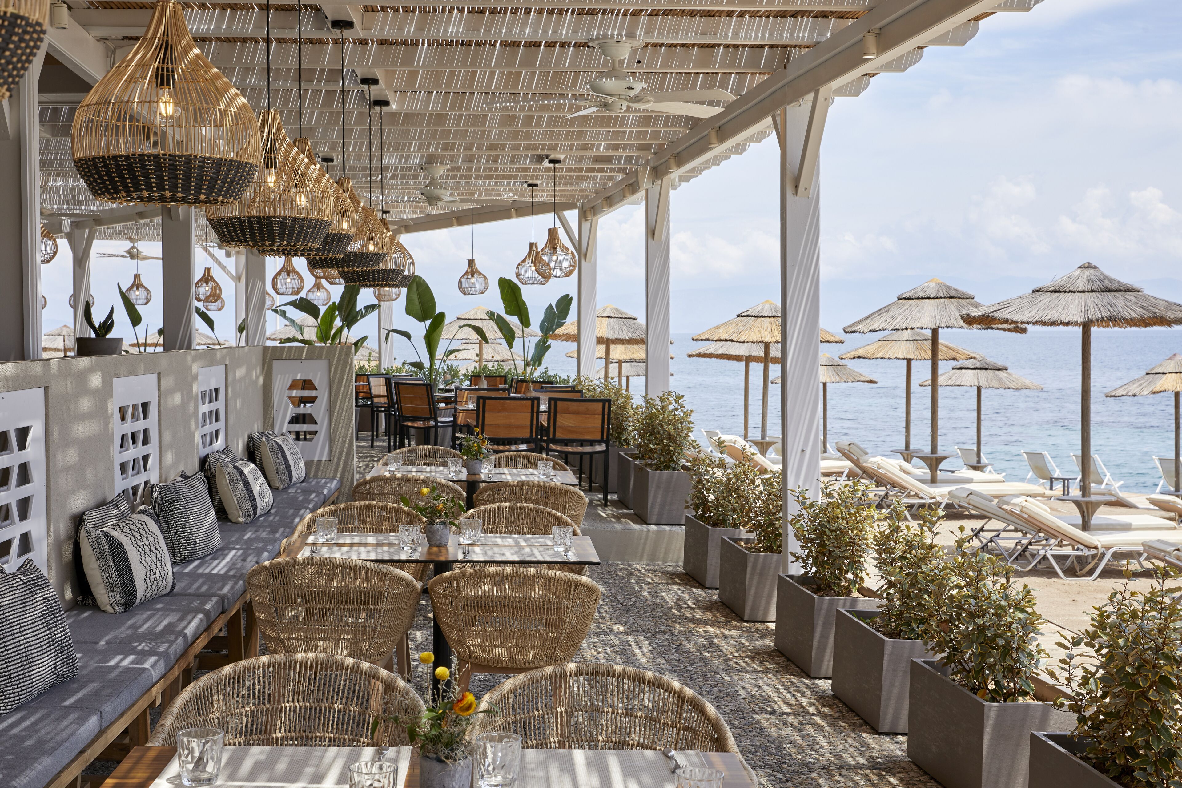 Un área de comedor exterior con mobiliario de mimbre y lámparas colgantes, con vistas al mar.