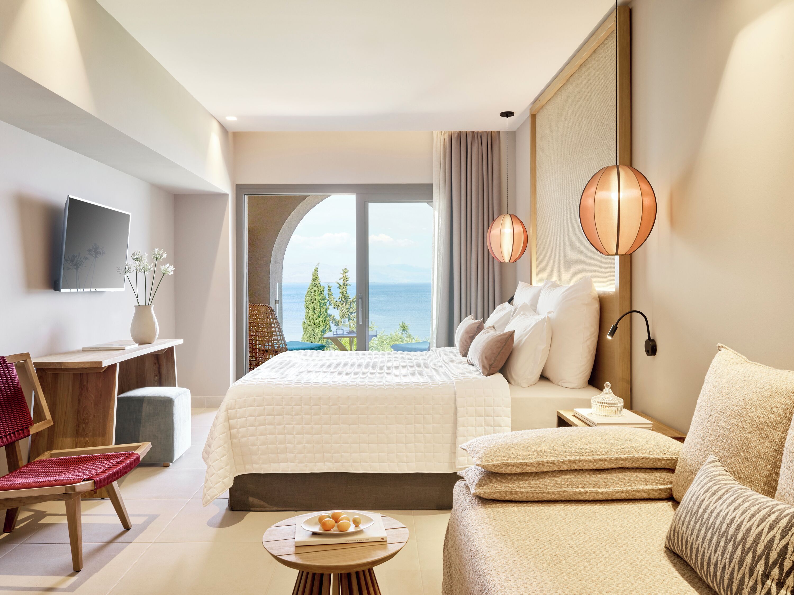 Une chambre d’hôtel moderne dotée d’un grand lit, d’un canapé, d’un bureau et offrant une vue sur la mer.