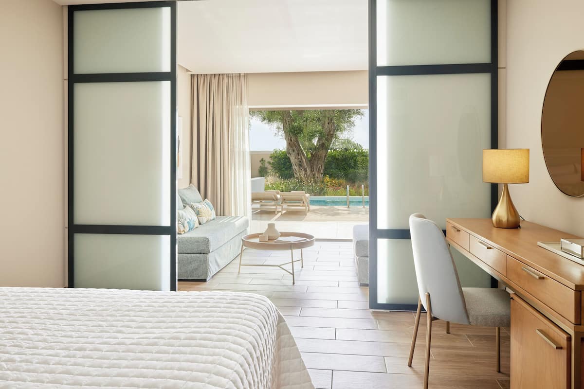 Ein modernes Hotelzimmer mit Bett, Schreibtisch, Stuhl und Blick auf einen Außenbereich mit Pool und Grünflächen.